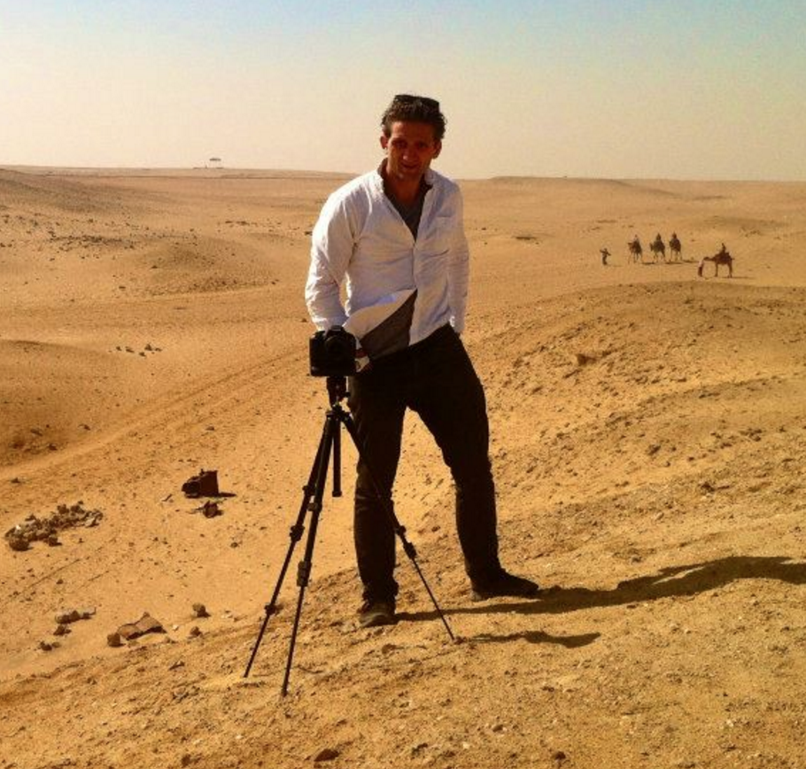 Self-portrait of Casey Neistat standing in front of a camera on a tripod atop a sand dune in the desert with camels in the background. Apparently taken during filming "Make It Count" for Nike.